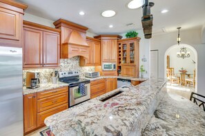 A kitchen with wooden cabinets, granite countertops, a built-in oven, and a dining area with a chandelier.