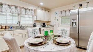 A kitchen with white cabinets, a stainless steel refrigerator, and a dining table set for four. - Peaceful Porch, Yard! Riverdale Home Near Dtwn ATL (Riverdale)