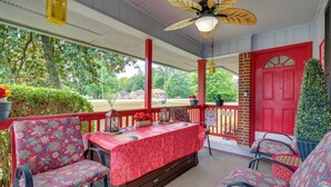 A covered porch with a table set for dining, surrounded by chairs, and a red door. - Peaceful Porch, Yard! Riverdale Home Near Dtwn ATL (Riverdale)