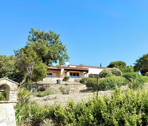 Una casa con un muro de piedra, una campana y un árbol grande al frente.