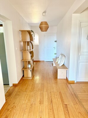 A hallway with wooden flooring, a wooden shelving unit, a hanging light fixture, and a white door.