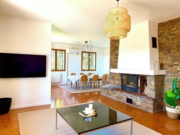 Una sala de estar moderna con chimenea de piedra, un comedor con mesa blanca y un televisor grande montado en la pared.
