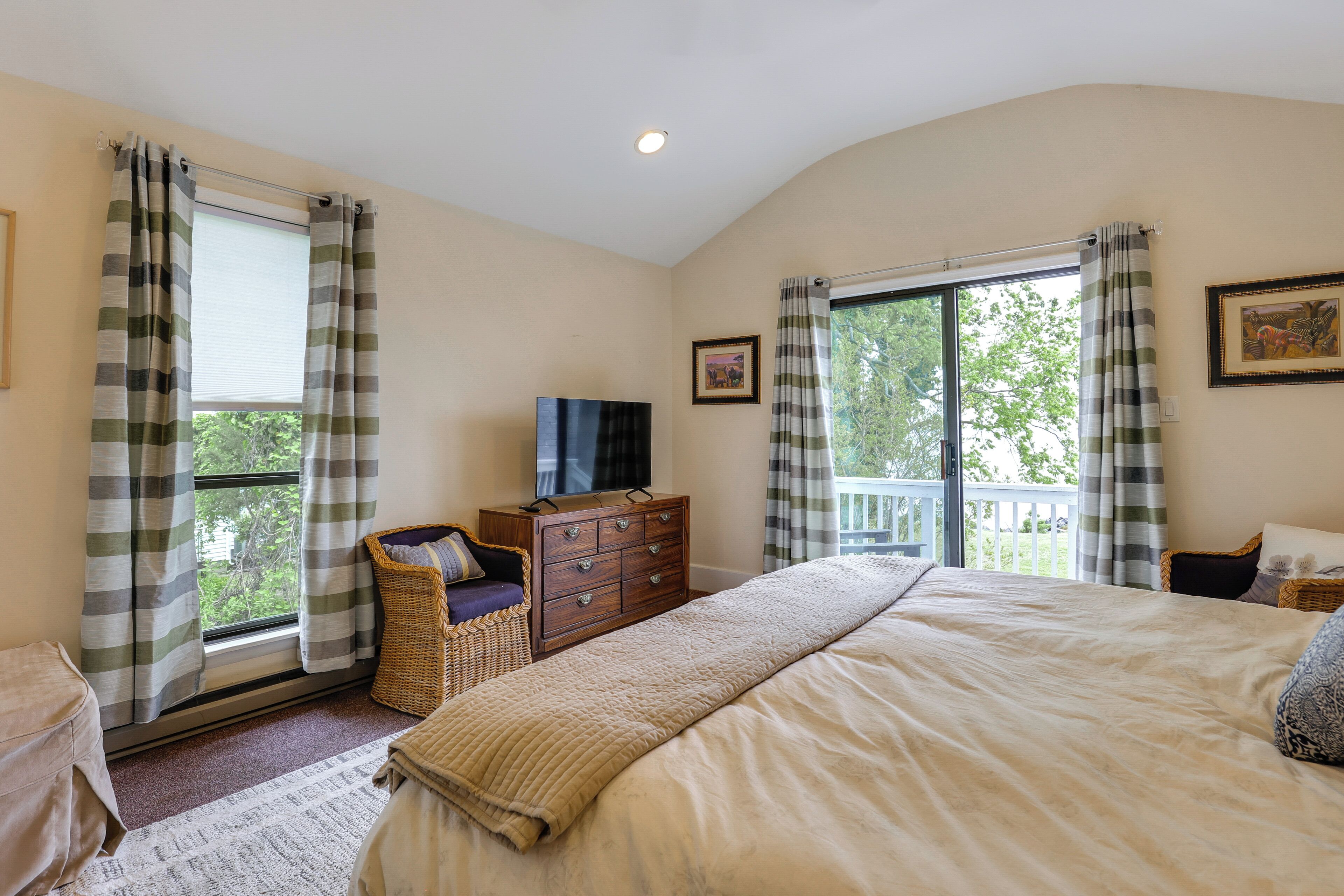 Une chambre à coucher comprenant un lit, une commode, un téléviseur et donnant sur l’extérieur.