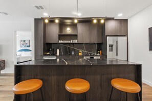 A modern kitchen with dark wood cabinets, a marble countertop, and three orange stools. - 6BDR, Brand New Hotel w/ Pool + Rooftop | The Code by AvantStay (Austin)