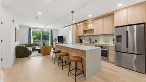 A modern kitchen with wooden cabinets, a stainless steel refrigerator, and a bar area with stools.