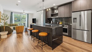 A modern kitchen with a central island, bar stools, stainless steel appliances, and a large window.