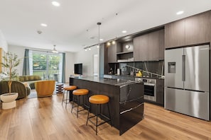 A modern kitchen with a central island, bar stools, stainless steel appliances, and a large window. - 6BDR, Brand New Hotel w/ Pool + Rooftop | The Code by AvantStay (Austin)