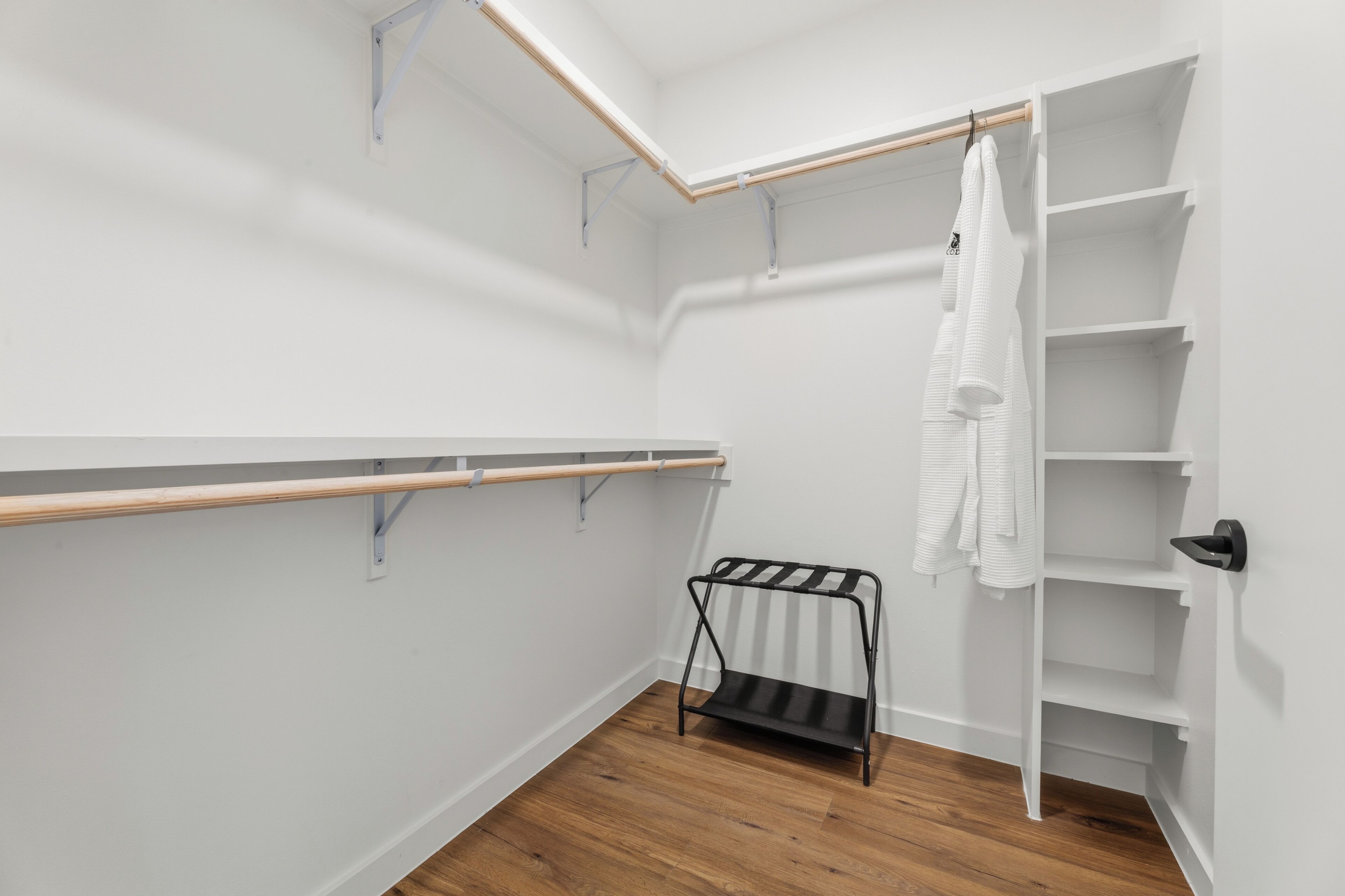 Ein begehbarer Kleiderschrank mit Holzboden, weißen Wänden und einem Metallgestell mit Kleidung.