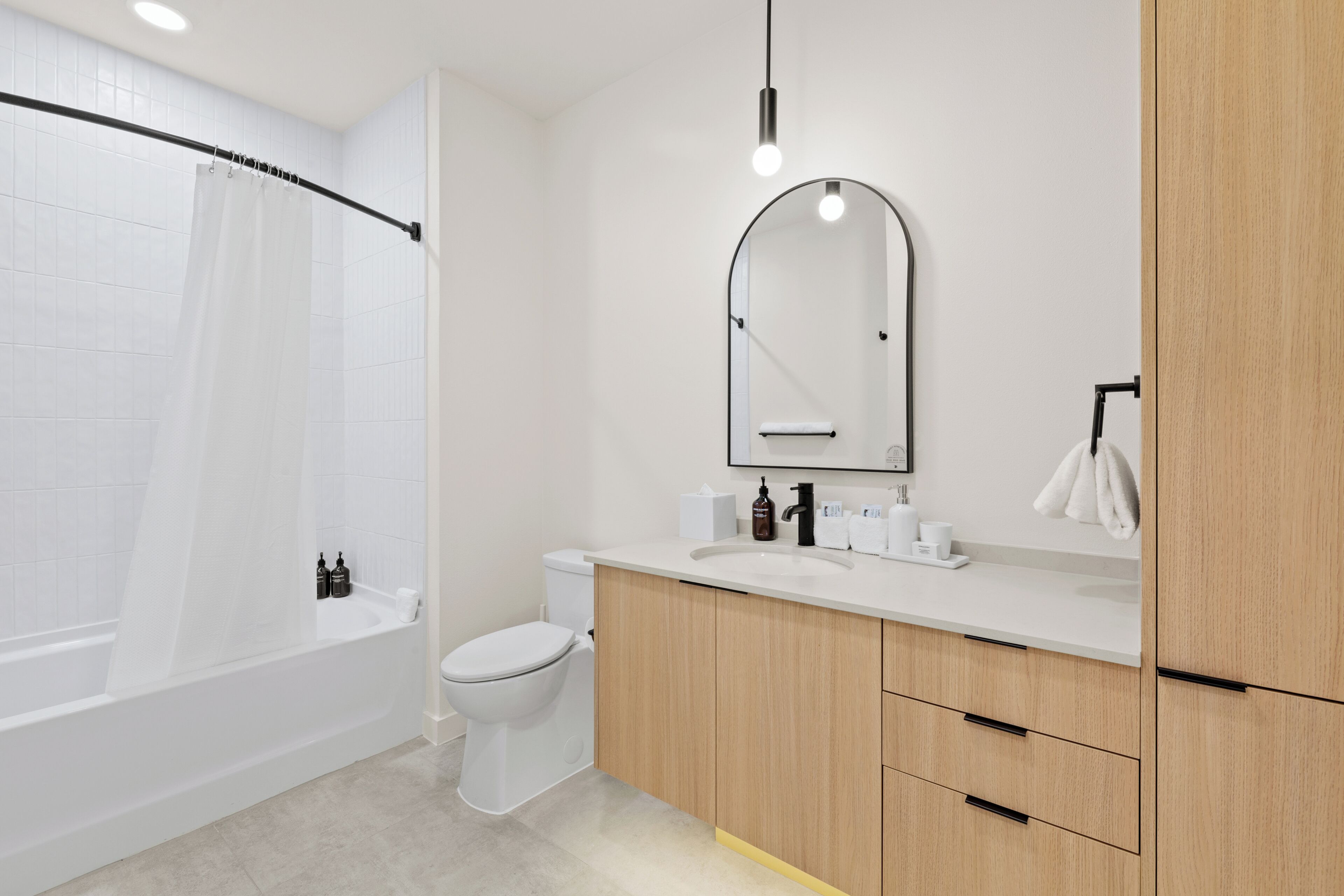 A modern bathroom with a bathtub, toilet, vanity with a mirror, and a shower curtain.