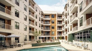 A modern multi-story hotel with balconies, a swimming pool, and outdoor seating areas.