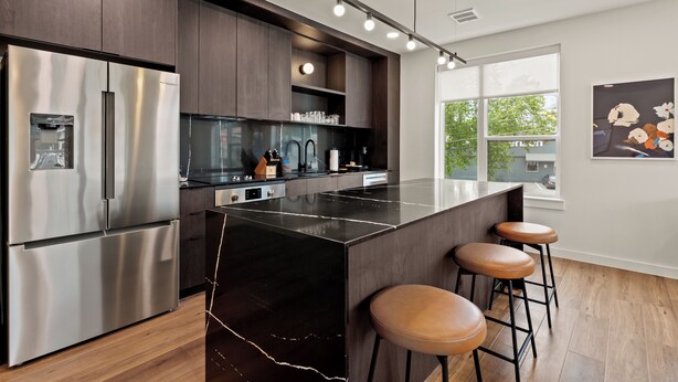 A modern kitchen with a stainless steel refrigerator, a black marble island, and wooden stools.