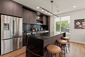 A modern kitchen with a stainless steel refrigerator, a black marble island, and wooden stools.