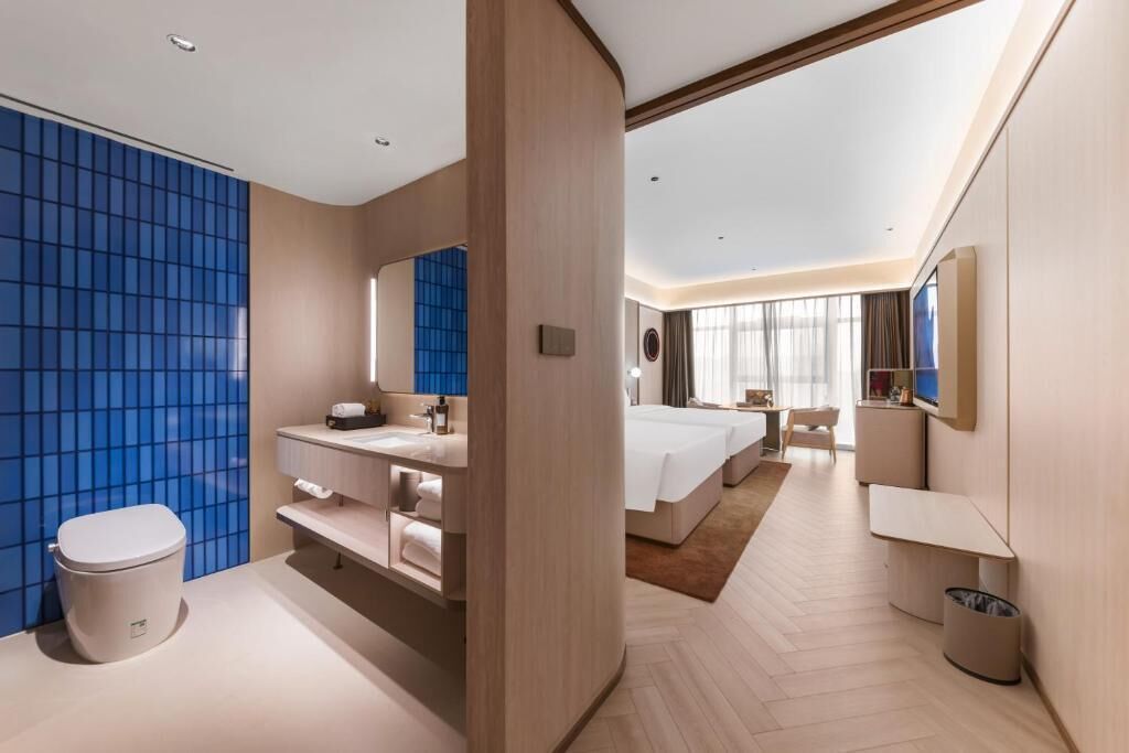 A modern hotel room with a large bed, a separate bathroom, a desk, and a large window.