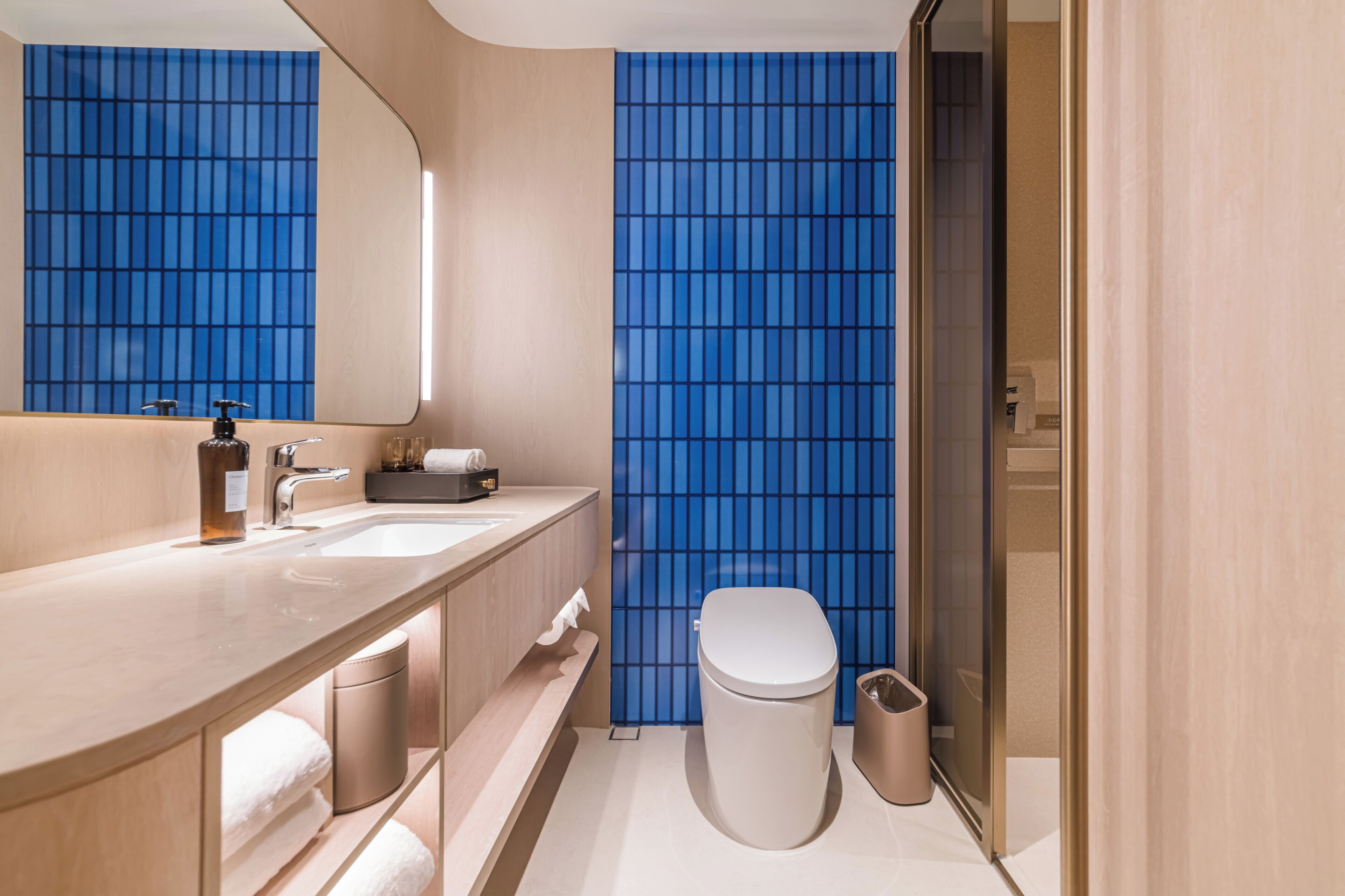 A modern bathroom with a vanity, sink, mirror, toilet, and trash can.