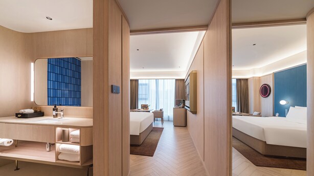 Ein Hotelzimmer mit großem Spiegel, Schminktisch mit Waschbecken, Bett, kleinem Schreibtisch und Blick auf die Stadt.