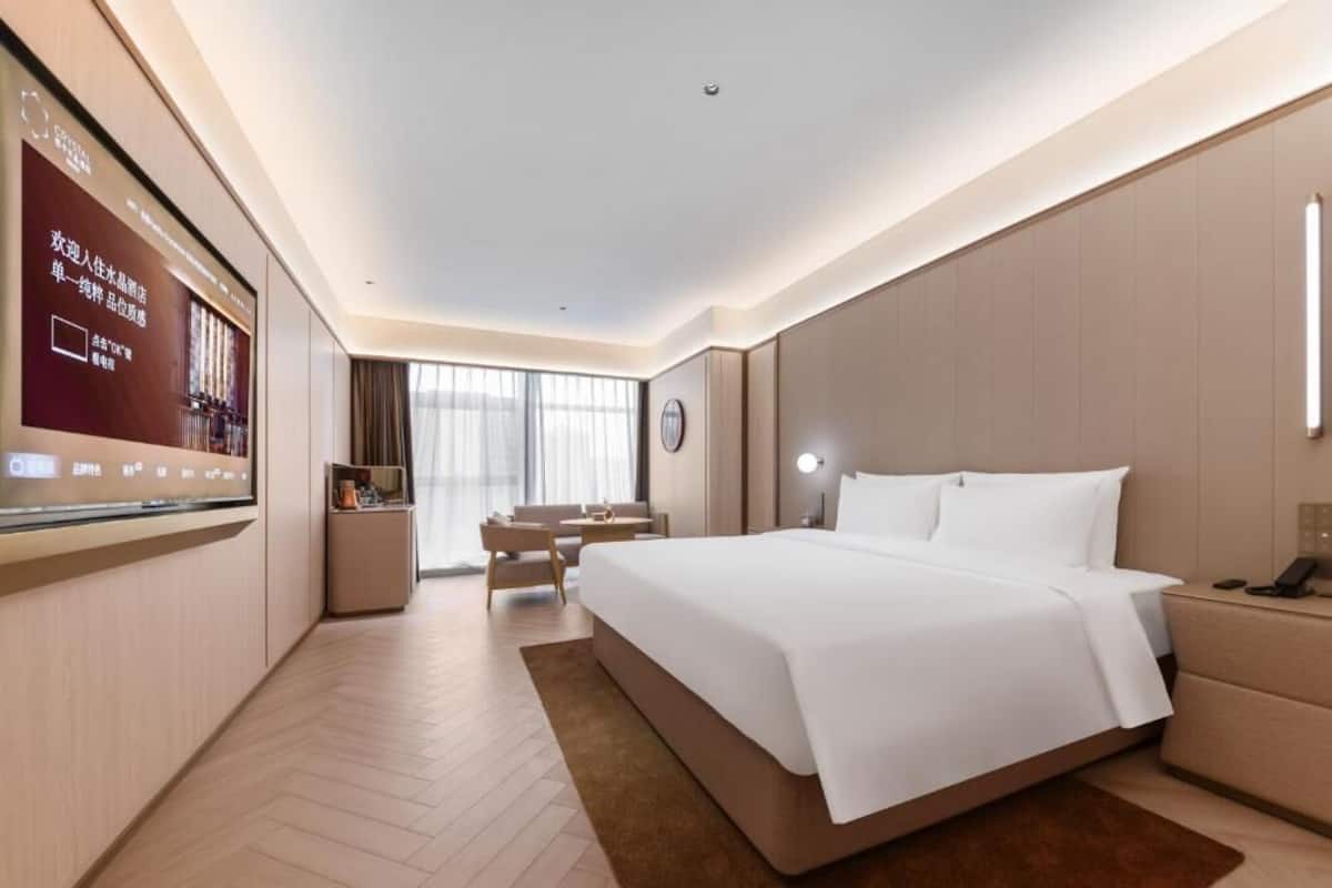 A modern hotel room with a large bed, a TV, a desk, and a seating area.