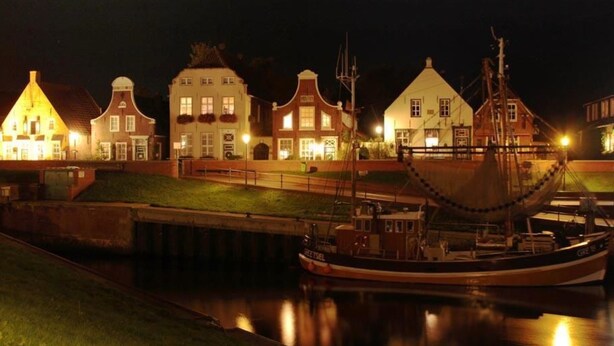 Un canal où un bateau est amarré, entouré de bâtiments traditionnels dont les fenêtres sont illuminées.