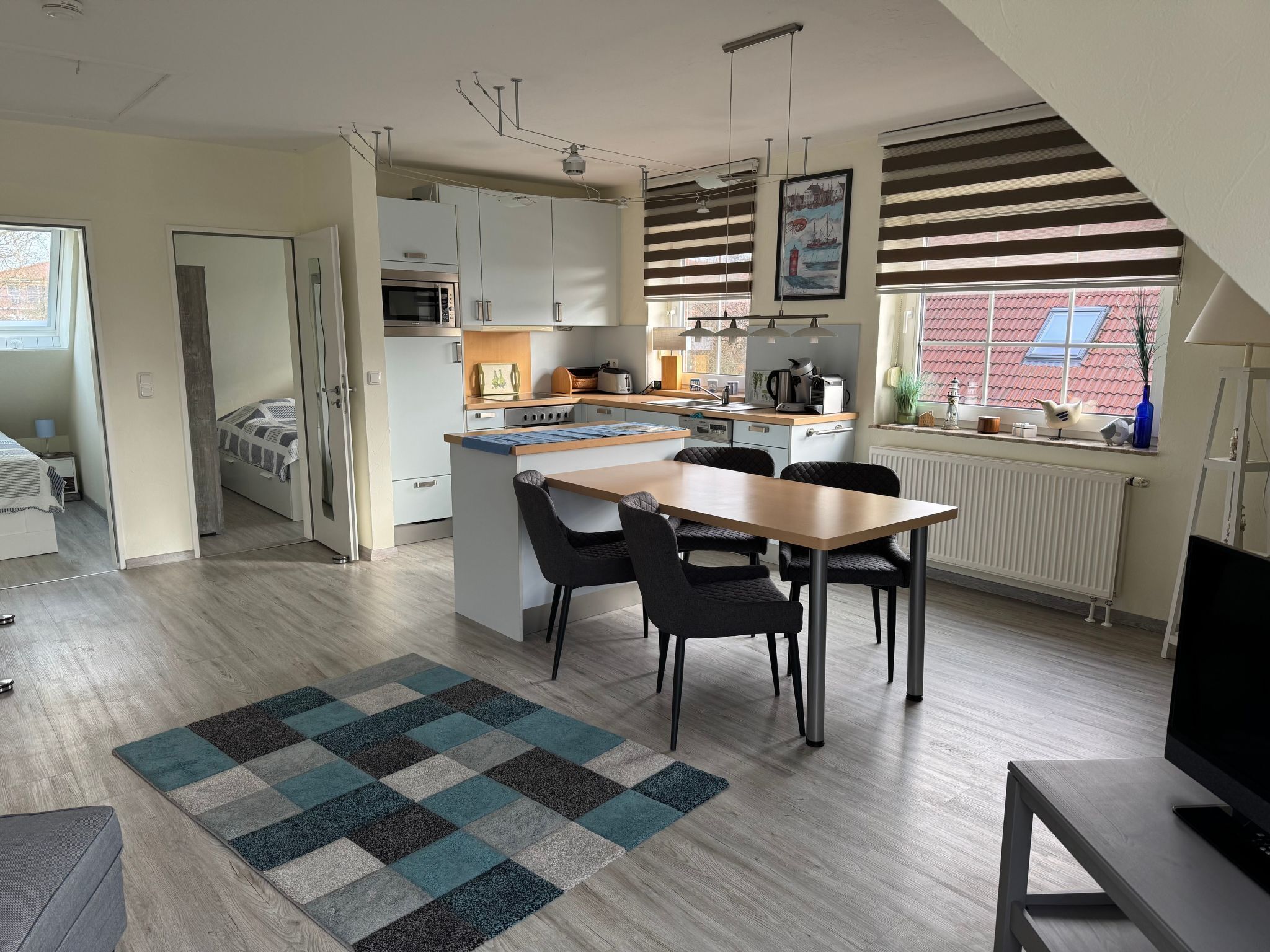 Een moderne keuken met een eethoek, een inbouwoven en een raam met uitzicht op een gebouw met rode dakpannen.