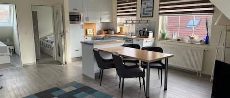 A modern kitchen with a dining area, a built-in oven, and a window with a view of a red-roofed building.