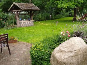 Jardí amb una glorieta de pedra, una boscaterra i una roca gran.