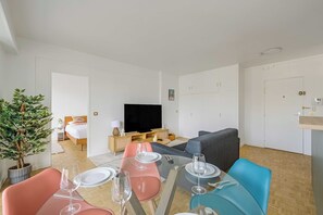 Ein modernes Wohnzimmer mit Esstisch für vier Personen, einer Couch, einem Fernseher und einer Zimmerpflanze.