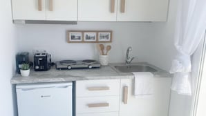 Une cuisine compacte avec des meubles blancs, un lave-vaisselle encastré, une machine à café, un grille-pain et un évier.