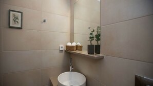 Un baño moderno con un espejo grande, un lavabo redondo y un estante con cestas y artículos de aseo.