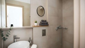 Un baño con lavamanos blanco, espejo, toallero, ducha y una planta pequeña.