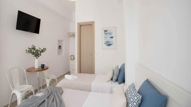 Habitación de hotel con cama, televisor montado en la pared, una mesita con una planta y una puerta.
