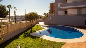 Ein Swimmingpool, umgeben von einem weißen Zaun, mit blauem Himmel und Gebäuden im Hintergrund.