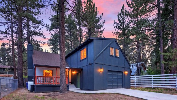 Una casa moderna de dos pisos con fachada oscura, un garaje visible y un porche con mobiliario exterior.