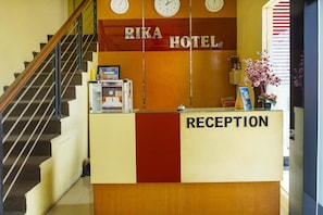 A reception desk with 'RIKA HOTEL' signage, a clock, and a staircase.