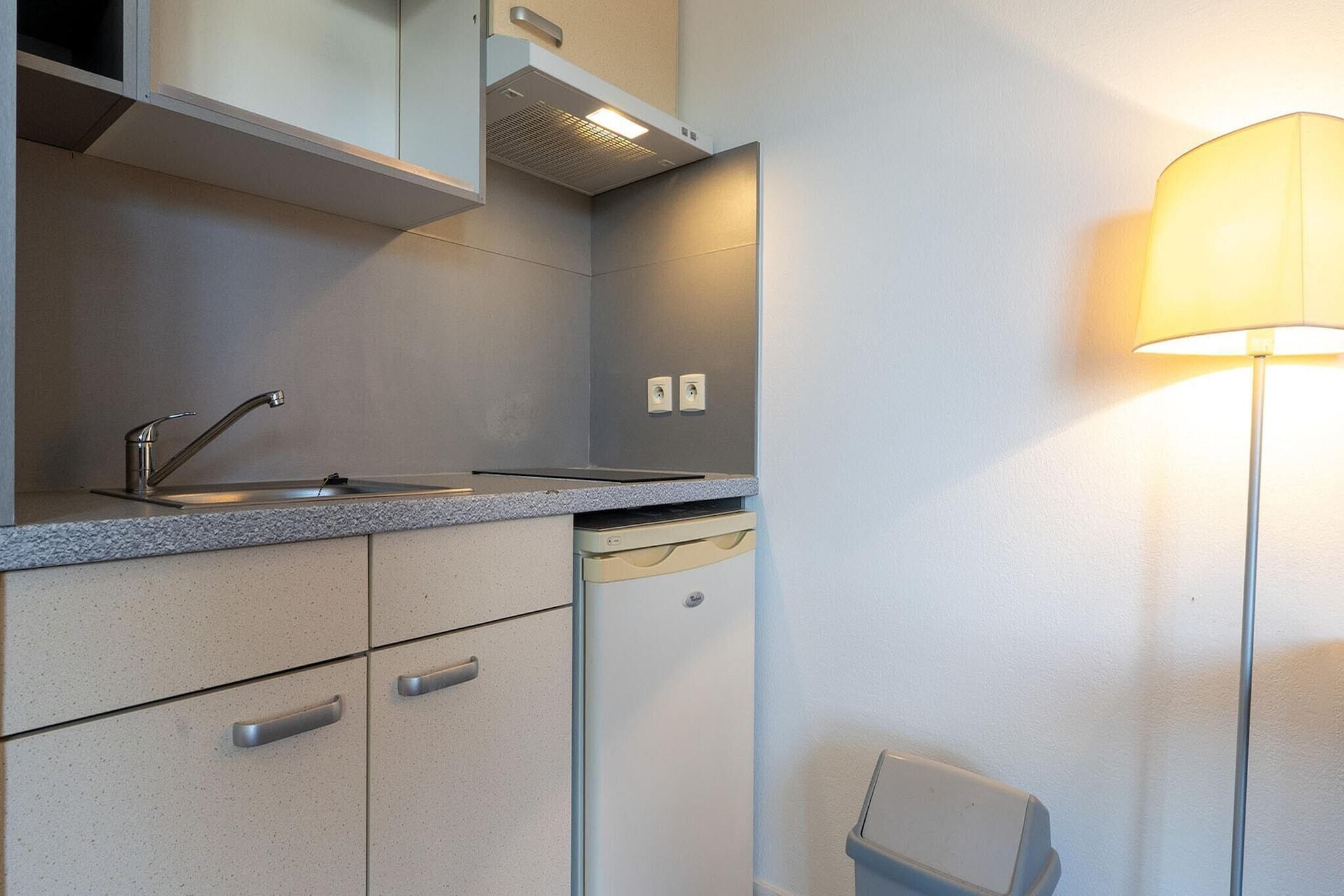 A compact kitchen with a built-in dishwasher, a sink, and a wall-mounted lamp.