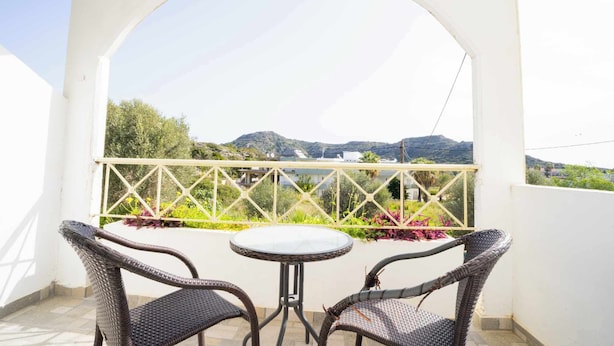Un balcon avec des fauteuils en osier et une table, offrant une vue sur un paysage montagneux.