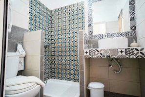 A bathroom with patterned tiles, a toilet, a sink, and a shower. - Farkia Exclusive Suites (Faliraki)