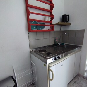 Uma cozinha compacta com fogão a gás, pia e escorredor de louça vermelho.
