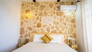 Une pièce avec un mur en pierre, un lit avec une literie blanche et une table de chevet avec une lampe.