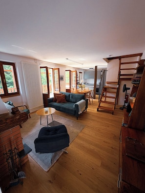 Ein großzügiger Wohnbereich mit einer Couch, einem Couchtisch und einem Esstisch. Eine Treppe führt zu einer oberen Ebene.