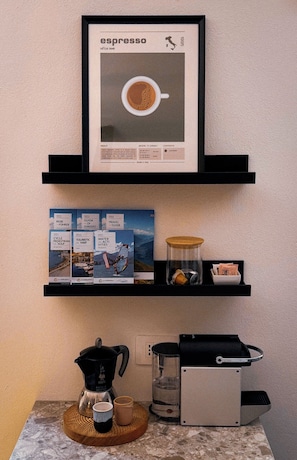 Ein gerahmter Espresso-Werbeplakat, Reiseführer, eine Kaffeemaschine, ein Wasserkocher und ein Wasserspender auf einer Küchenarbeitsplatte.