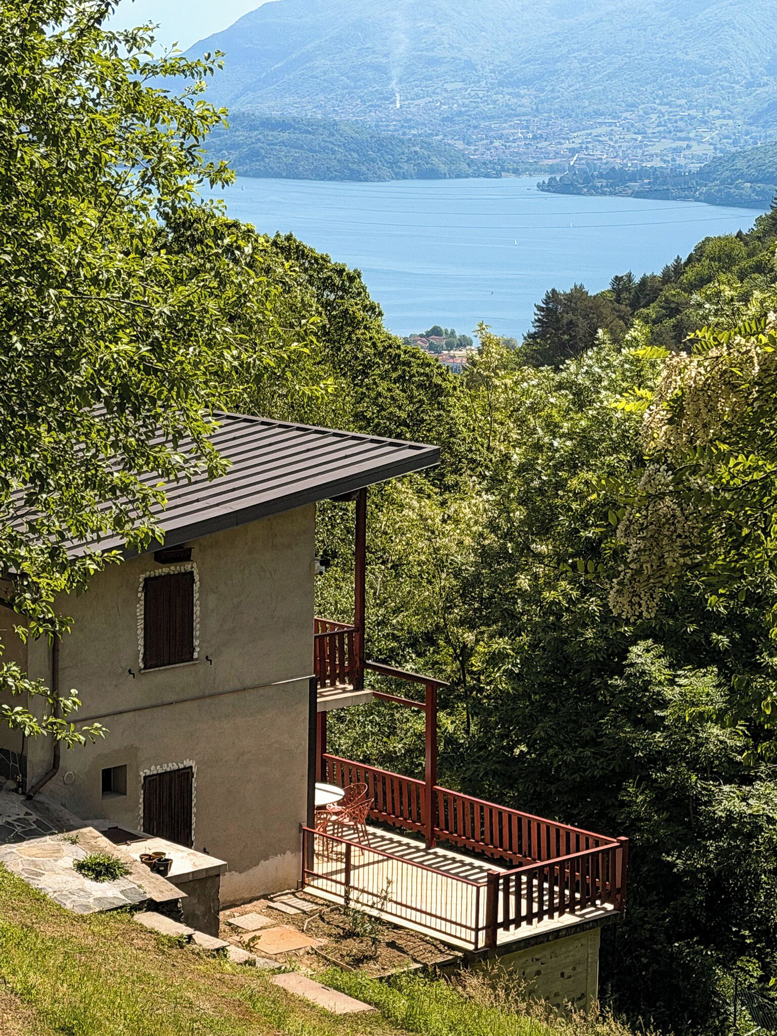 A two-story building with a balcony, surrounded by lush greenery and a lake view.