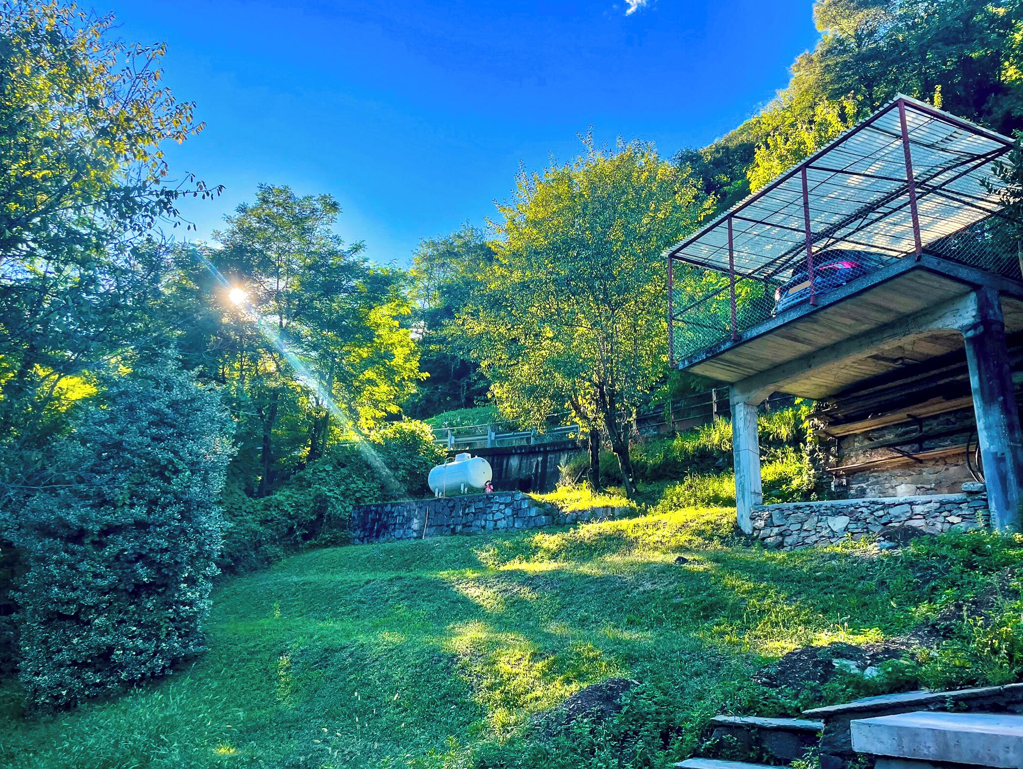 A lush garden with a stone wall, a metal structure, and a large white tank.