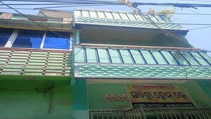 A multi-story building with a green facade, a balcony with a metal railing, and a sign with text in a non-Latin script. - Sabitri Homestay (Puri)