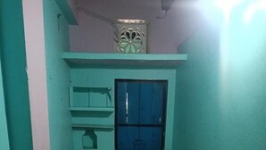 A small, narrow room with a bed, a window with a decorative grille, and a tiled floor. - Sabitri Homestay (Puri)