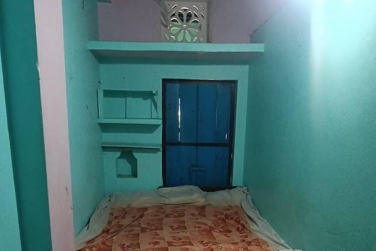 A small, narrow room with a bed, a window with a decorative grille, and a tiled floor.