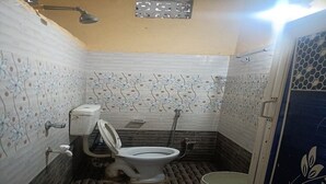 A small bathroom with a toilet, a shower, and a bucket. - Sabitri Homestay (Puri)
