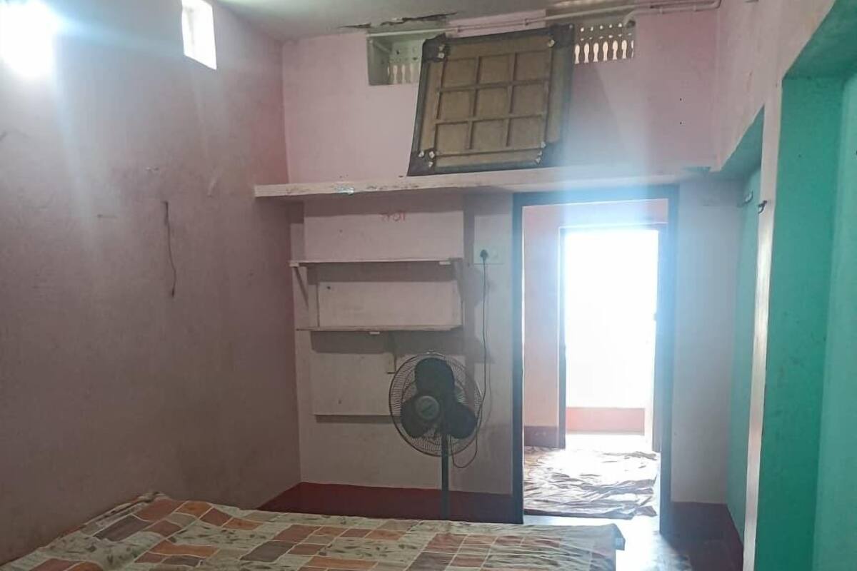 A bedroom with a bed, a ceiling fan, a standing fan, a window, and a door leading to another room.