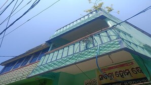 A multi-story building with a green facade, a balcony on the upper floor, and a sign with text. - Sabitri Homestay (Puri)