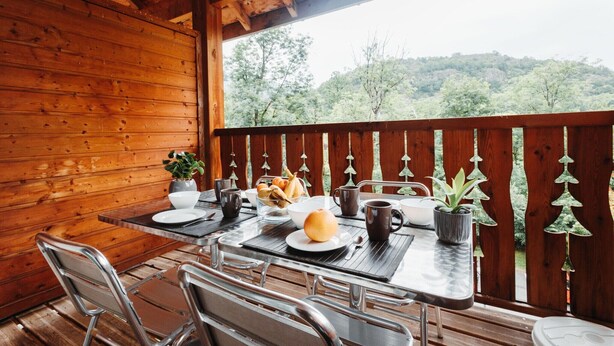 A wooden deck with a table set for breakfast, surrounded by metal chairs, and a view of a forested hillside. - Apartment for 4 near the Gondola (Ax-les-Thermes)