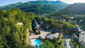 An aerial view of a resort with multiple buildings, a swimming pool, and surrounding forested hills. - Rental for 6 with Private Balcony (Ax-les-Thermes)