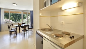 A compact kitchen with a sink, two burners, and a dining area with chairs and a table. - Studio in the Heart of Nature (Vallon-Pont-d’Arc)